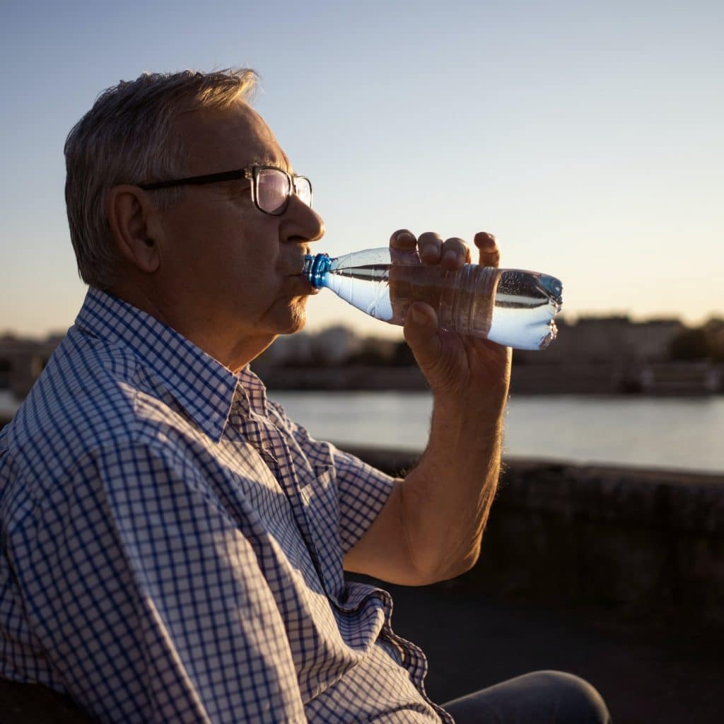 homme agé bois de l'eau dans une bouteille