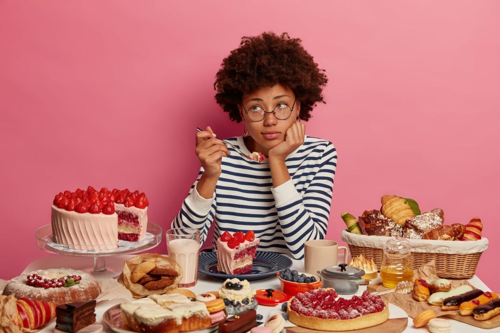femme entourée de gâteaux l'ai pensive. Elle se demande si les glucides font grossir