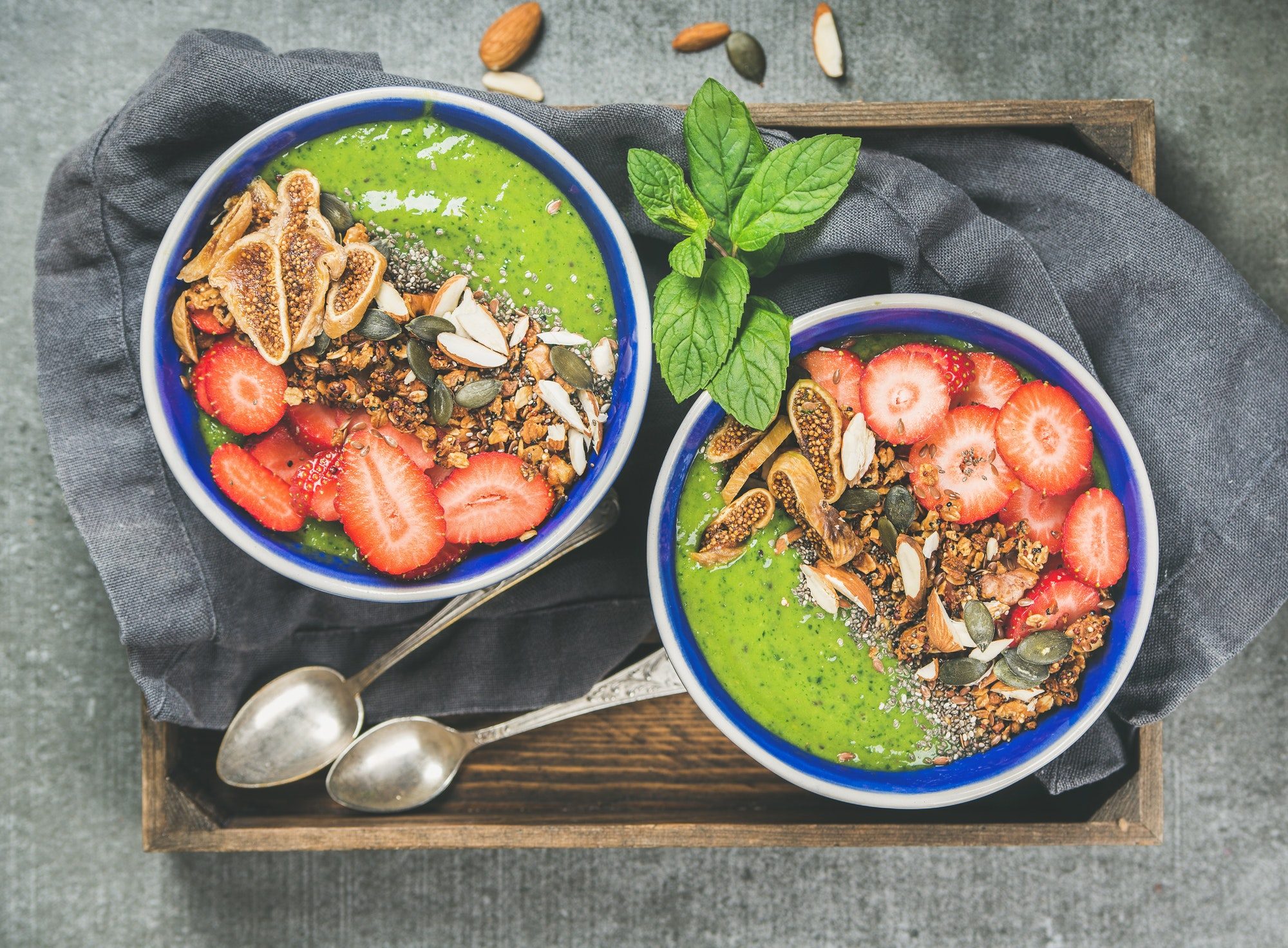Healthy green smoothie breakfast bowls with granola, fruit, seeds, berries
