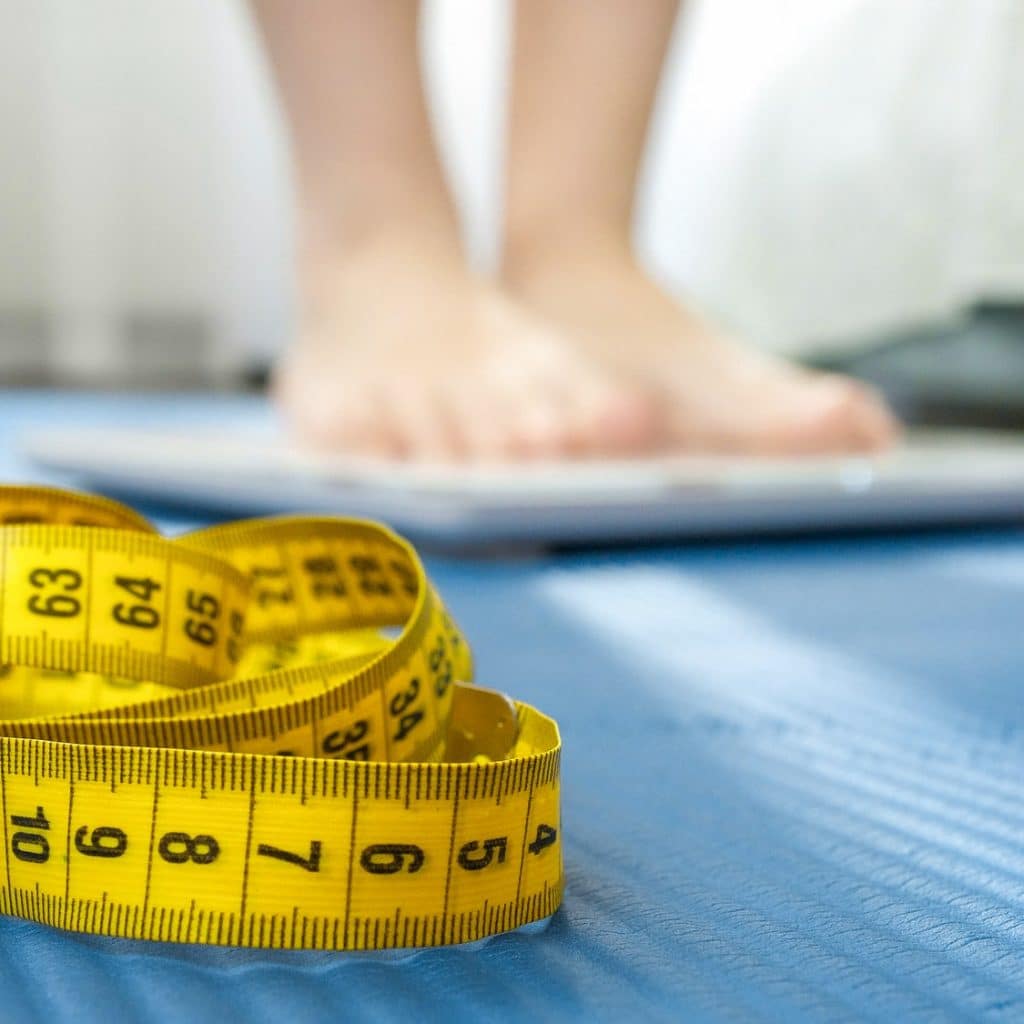 Measuring tape, fitness mat and young woman weighting on scales. Concept of dieting, sports, loosing