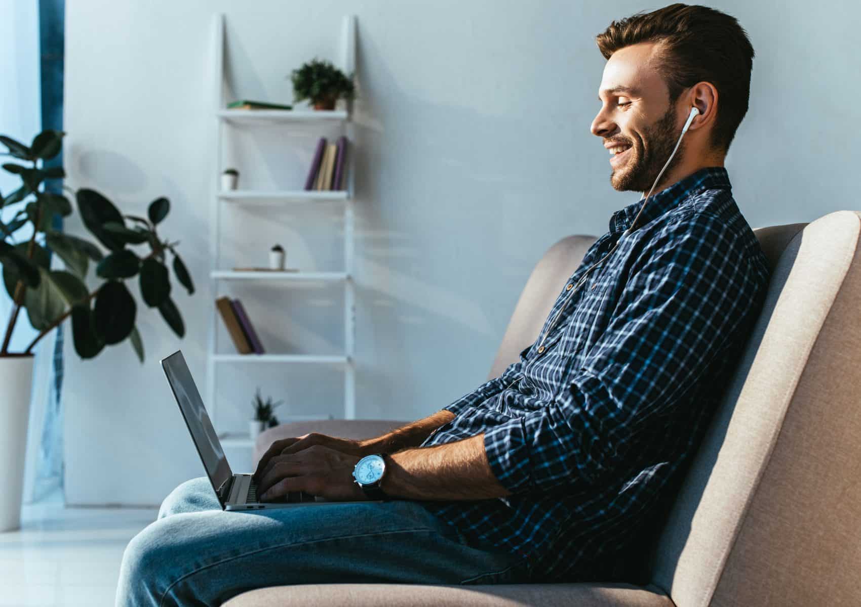 side view of smiling man in earphones taking part in webinar at home