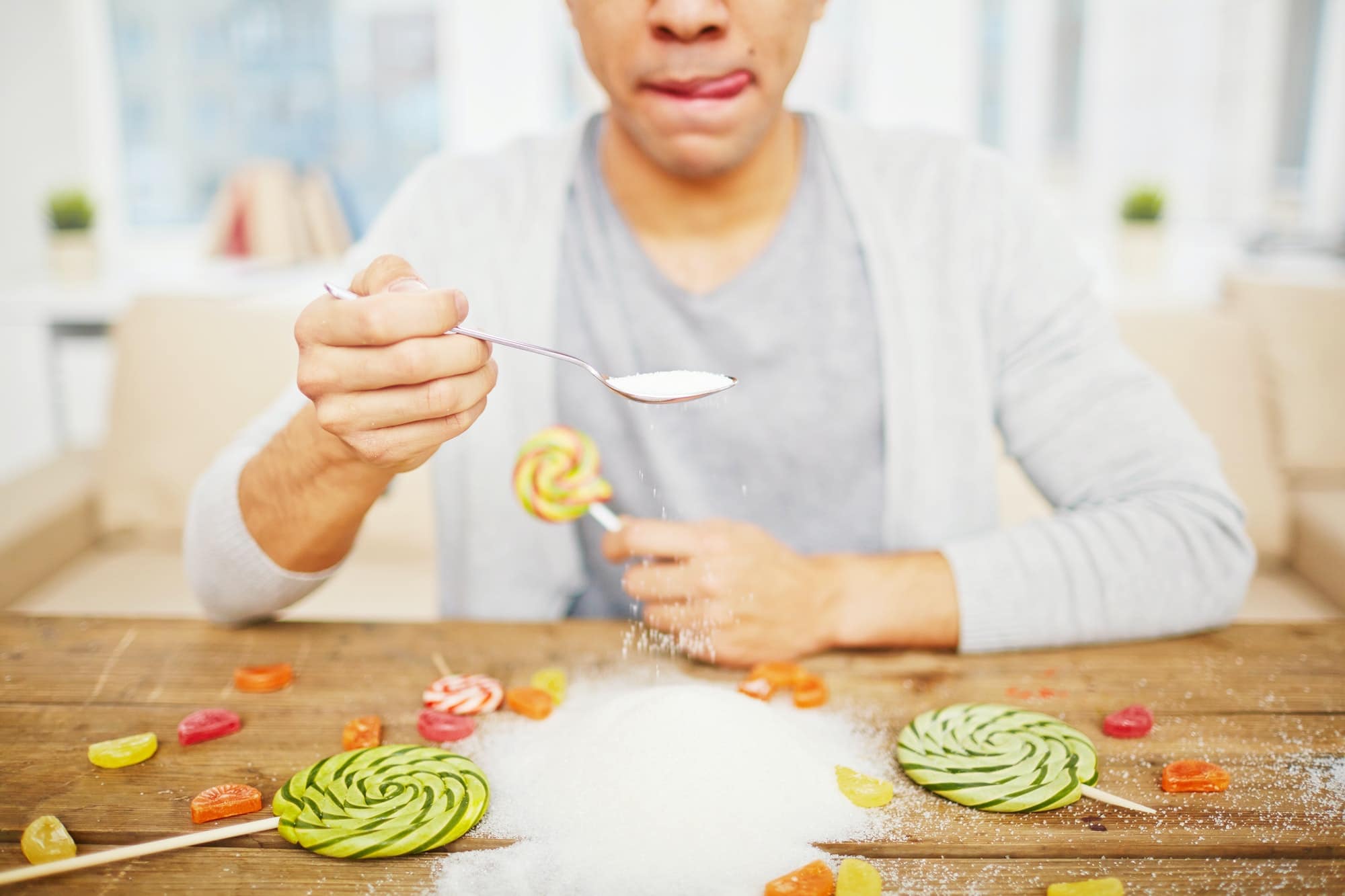 man holding a spoonful of sugar. lolipops on the table