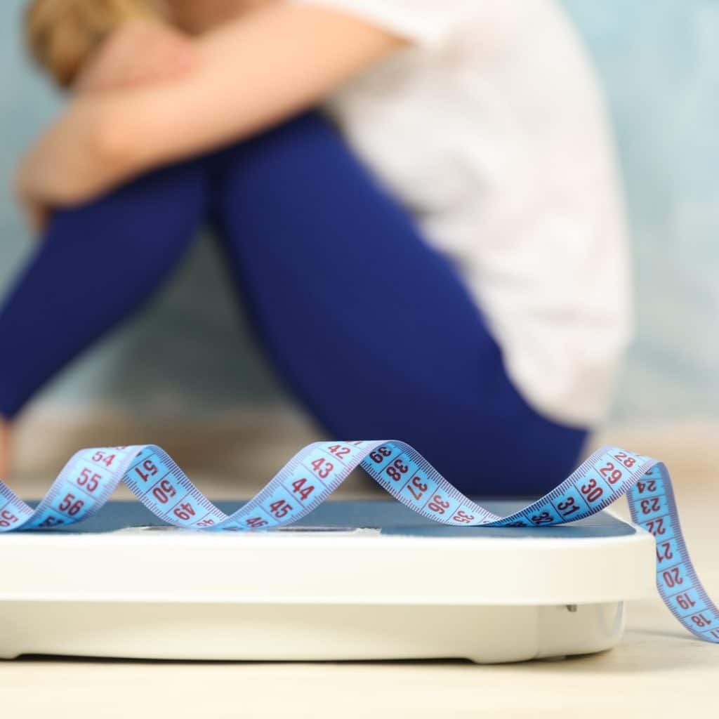 sad woman sitting next to a scale and measuring tape