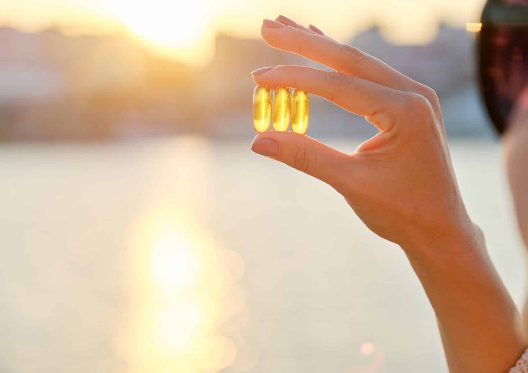 Yellow gel capsule vitamin d omega-3 in womans hand, sun sea background